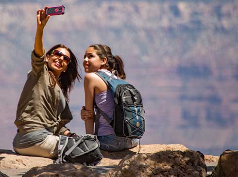 Mother and daughter seated along the Canyon's cliff edge taking a selfie during Hermits Rest Sunset Tour