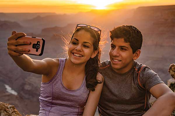 Teenagers taking selfie at Grand Canyon with sunset behind them