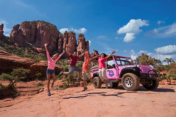 Family jumping on Sedona red rocks with Pink Jeep in background