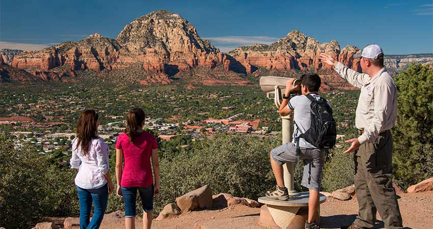 Pink Jeep guide pointing out Thunder Mountain with boy looking through telescope at Sedona's Airport Mesa Overlook