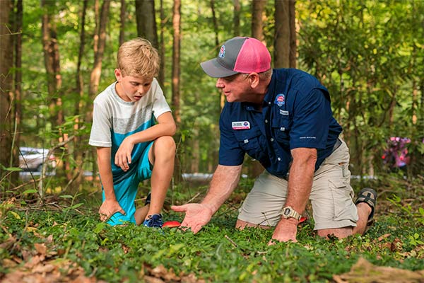 Pink Jeep guide kneeling on ground showing young boy wild mushrooms, Roaring Fork Smoky Mountains Tour