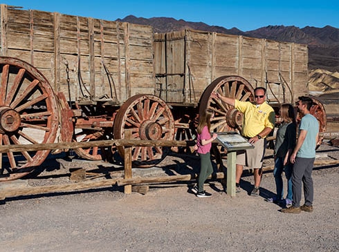 Pink Adventure Death Valley Tour guide and guests talking next to Twenty-Mule Team Wagon at Harmony Borax Works