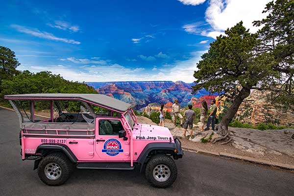 Pink Jeep Tours vehicle parked at beautiful Grand Canyon South Rim overlook, with tour guide and guests standing near rim