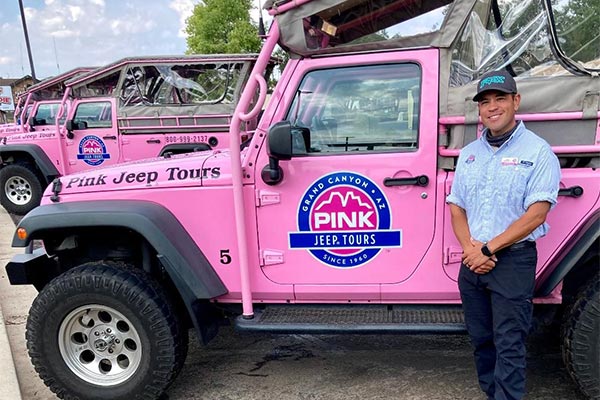 Pink Jeep Adventure Tour Guide Jason Rodriguez posing beside a row of parked Pink Jeep Wranglers.