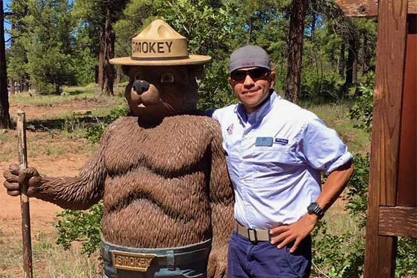 Pink Jeep Tour guide Jason Rodriguez posing with statue of Smoky the Bear near Arizona's Grand Canyon.