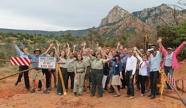 Oak Creek Schnebly Hill Road Erosion Project team members strike a celebratory pose with Sedona Red Rock formations in background.