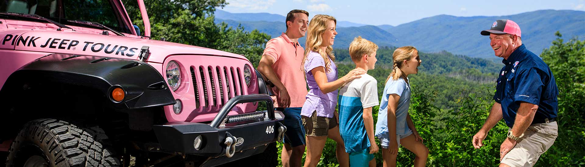 Pink Jeep tour guide laughing with guests next to jeep with clear summer view of Smoky Mountains in background.