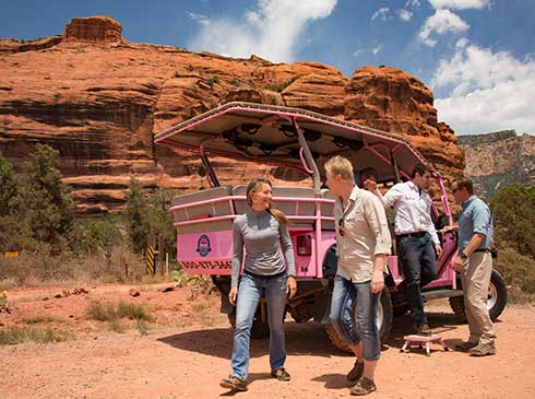 Tour guests exiting Pink® Jeep® vehicle with Sedona's large red rock formations in background