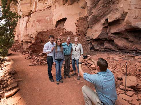Pink® Jeep® guide taking photo of four guests standing by cliff dwellings at Honanki Heritage Site near Sedona