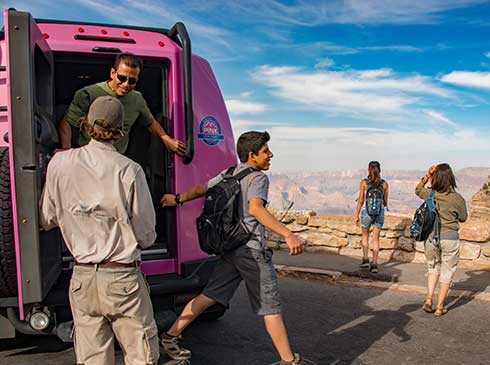 Grand Canyon South Rim tour guests exiting the back of Pink Jeep Tour Trekker with guide at canyon viewpoint.