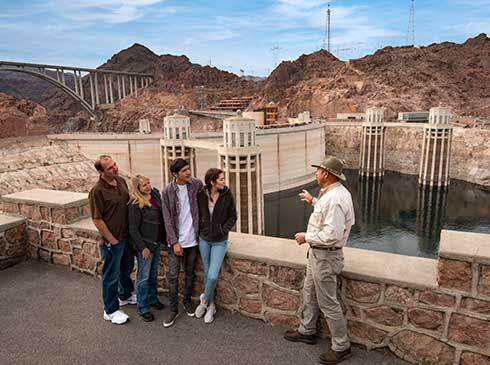 Pink Jeep guide explaining history of Hoover Dam to guests with view of dam spillway