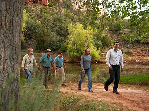 Pink® Jeep® guide and four guests walking along a heavily-vegetated trail past lower Oak Creek, near Sedona, AZ