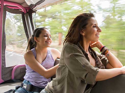 Smiling mother and daughter looking at roadside views from a Pink® Jeep® Wrangler