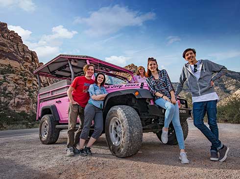 Fun group photo of tour guests posing on Pink Jeep Tour Trekker vehicle at Red Rock Canyon
