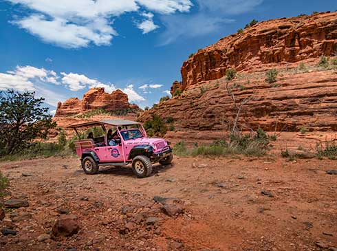 Custom Pink® Jeep® Wrangler with guests traveling the Broken Arrow Trail past large red rock formations