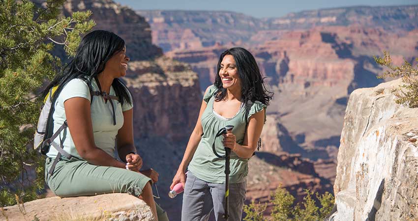 Two women resting along the Grand Canyon's Hermit Trail with the canyon rock formations in the background.