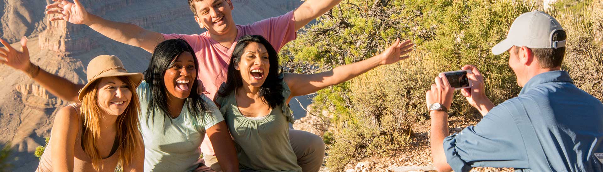 Pink Jeep® Tours Adventure guide taking a photo of four women posing with the Grand Canyon in the background.