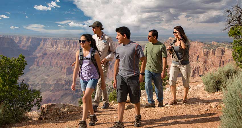 Pink Jeep Tour's adventure guide walks along the edge of the South Rim with a family of four with the canyon landscape in the background.