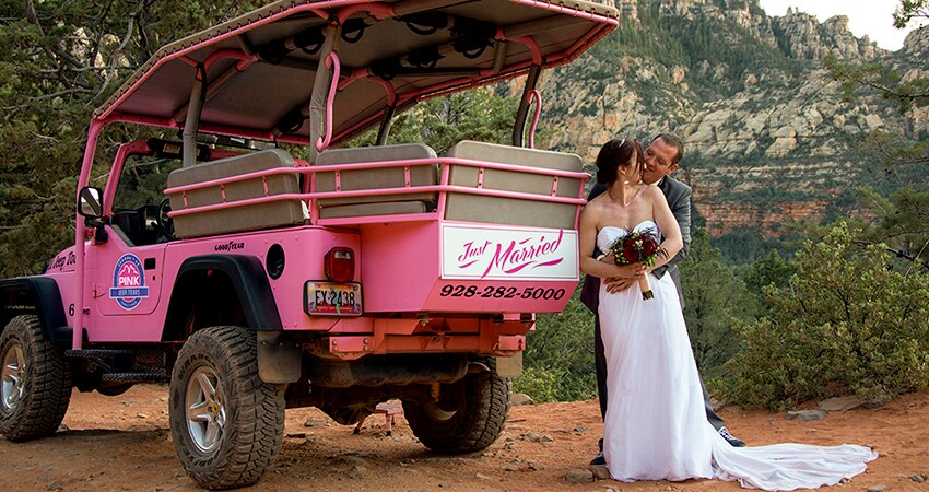 Bride and Groom kissing behind "Just Married" Pink Jeep