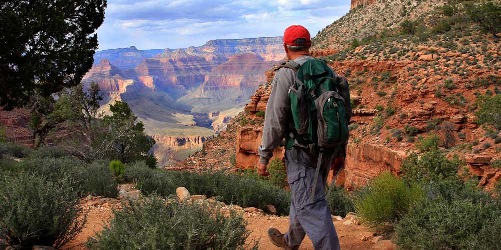 GC_Hiking.jpg Rear view of hiker with backpack as he walks on a dirt trail toward a view of the Grand Canyon South Rim.