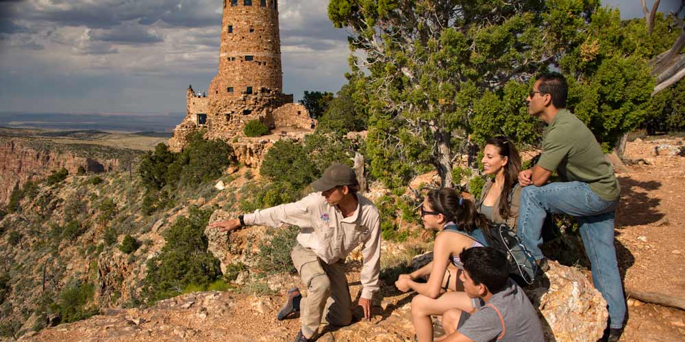 GC_Watchtower.jpg Pink Adventure tour guide kneeling beside seated guests and pointing towards Grand Canyon, with Desert View Watchtower in background.