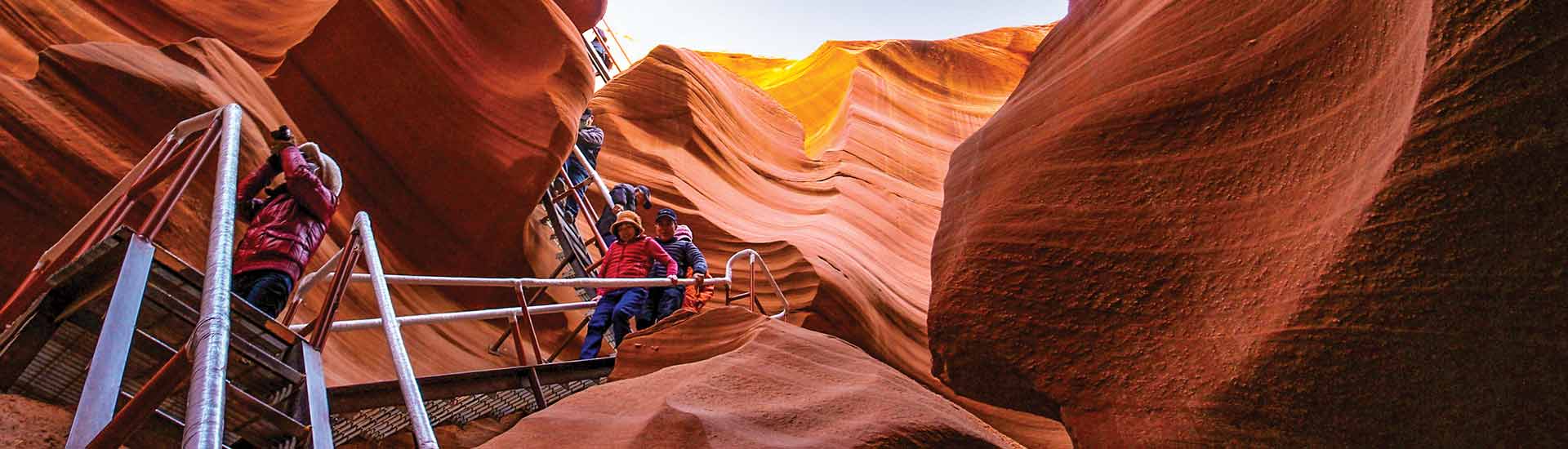 Visitors descending the staircase into Lower Antelope Canyon surrounded by swirling rock formations.