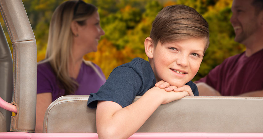 Young boy looking at camera from the back of a Pink Jeep with parents and the Smoky Mountains in background.