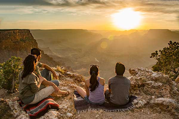 Four people seated on Grand Canyon rim viewing the sunset