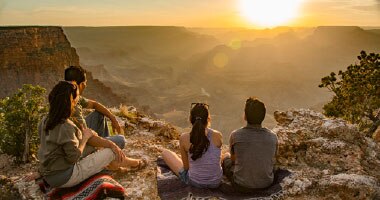 Parents and two kids seated on Grand Canyon South Rim looking out towards a golden sunset.