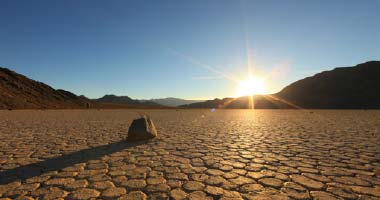 Sunset view of Racetrack Playa in Death Valley National Park with sand dunes in the distance.