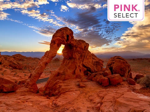 Sun setting behind Elephant Rock, Valley of Fire State Park, NV with blue sky clouds and Pink Select tour logo.