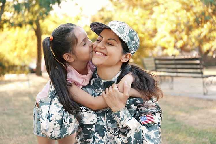Daughter hugging and kissing mother in military uniform.