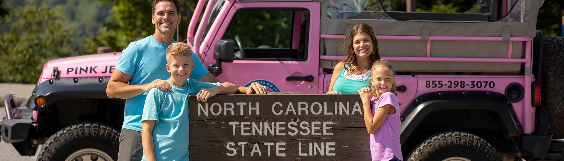 Family of four on Pink Jeep Newfound Gap tour posing at North Carolina-Tennessee state line sign, GSMNP