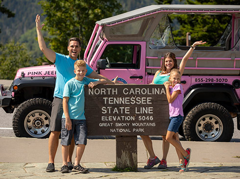 Pink Jeep Newfound Gap tour guests posing at North Carolina-Tennessee state line sign, GSMNP