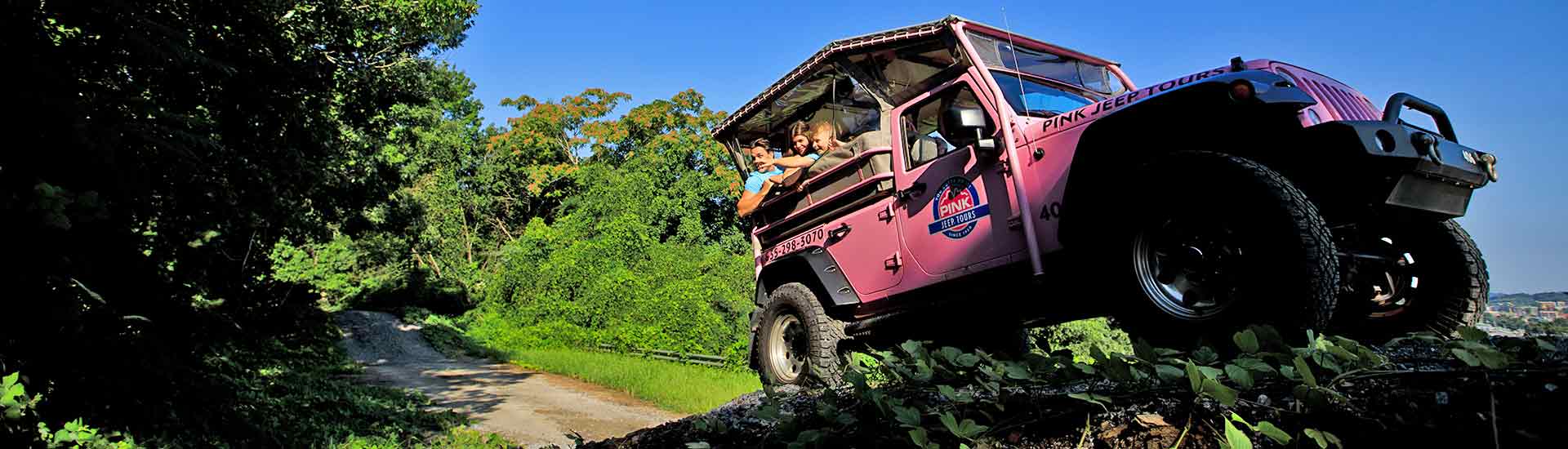 Pink Jeep climbing steep hill surrounded by lush green forest and blue sky with late afternoon shade, Pigeon Forge