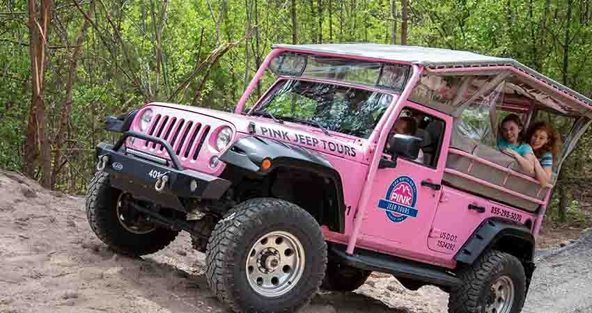 Close-up of Pink Jeep Smoky Mountains tour vehicle climbing steep dirt trail with ladies riding in back