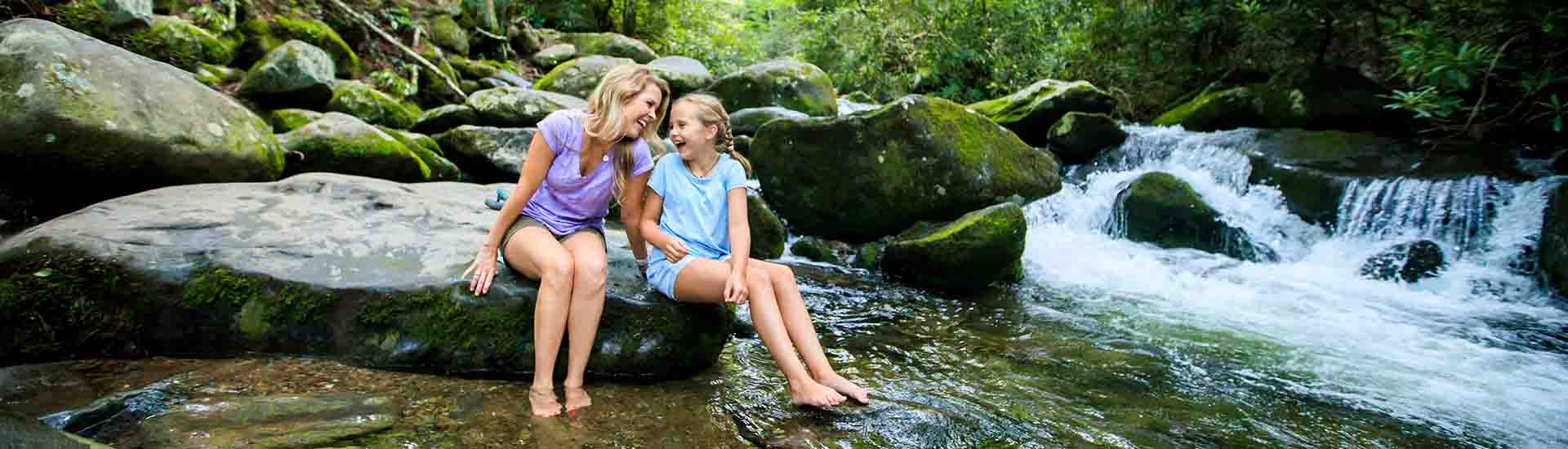 Mother and daughter seated with feet in mountain stream on Pink Jeep Tours Roaring Fork Smoky Mountains tour