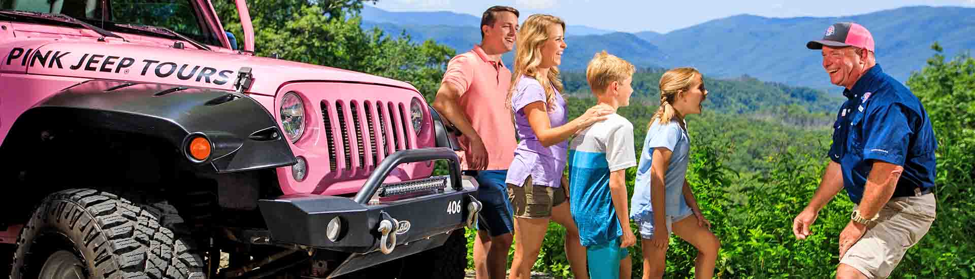 Pink Jeep tour guide laughing with guests next to jeep with clear summer view of Smoky Mountains in background