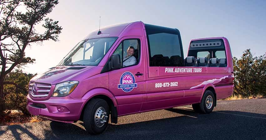 Pink® Adventure® Tours' certified guide in driver's seat of open-air PanoramaVan® with blue sky at twilight