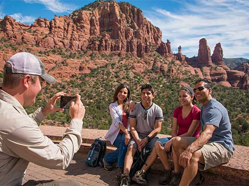 Pink Jeep guide taking photo of family seated on Chapel of Holy Cross platform with Twin Sisters rocks in back