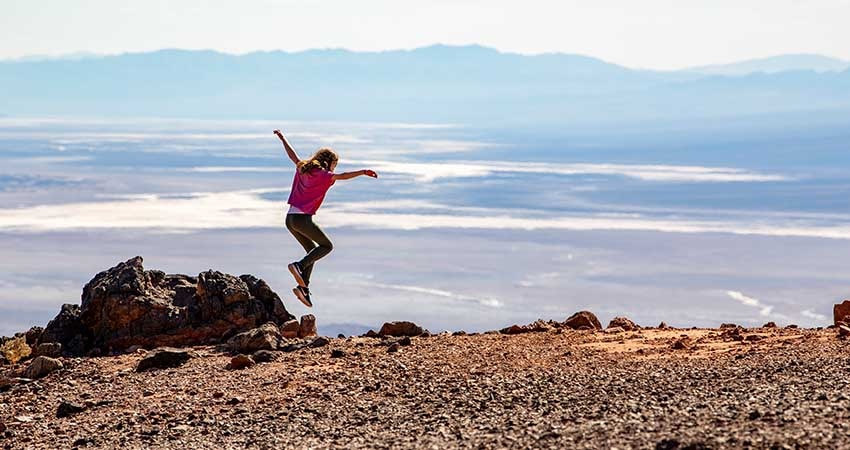 Young girl leaping into air with Death Valley salt flats and mountains in background, Pink Adventure Tour's Death Valley tour