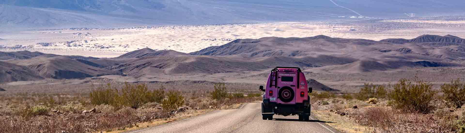 Rear end of Pink Adventure Tour Trekker driving towards the hills and slat flats of Death Valley National Park
