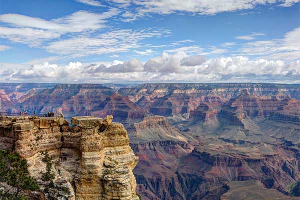 View of Mather Point overlooking geological formations of Grand Canyon South Rim, puffy white clouds in blue sky