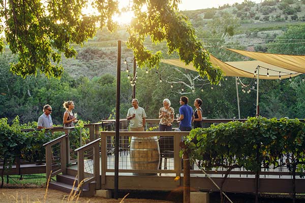 Pink Sedona Wine Tour guests enjoying a tasting on the creekside vineyard deck at Page Springs Cellars Winery, Verde Valley, AZ.