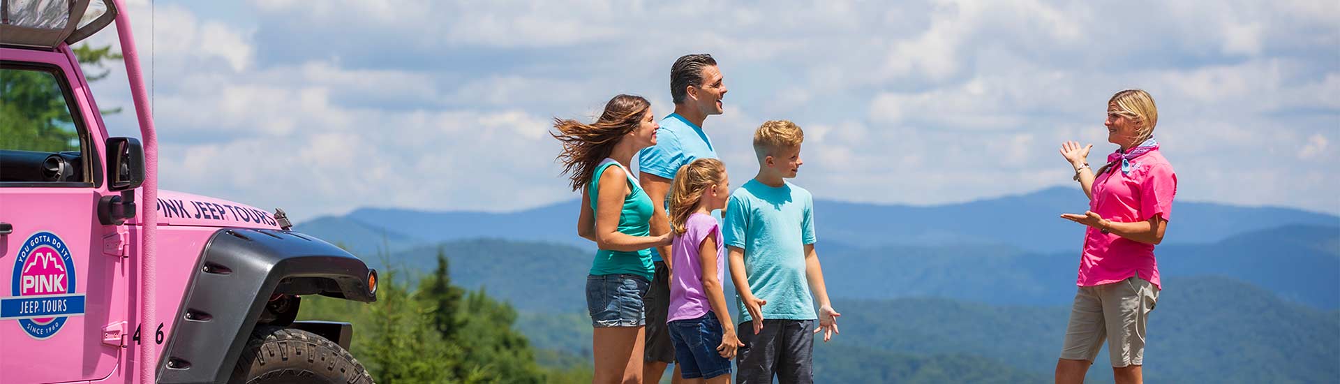 Pink Adventure Tours guide talking with family at a Smoky Mountains scenic viewpoint with a Pink Jeep Wrangler in the foreground.