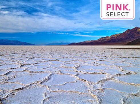 Closeup of white salt flats at Death Valley National Park with mountains in the distance, with Pink Select logo overlay.