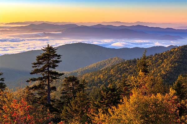 The sun rises over the Smoky Mountains at Clingmans Dome with brightly colored autumn trees in the foreground.