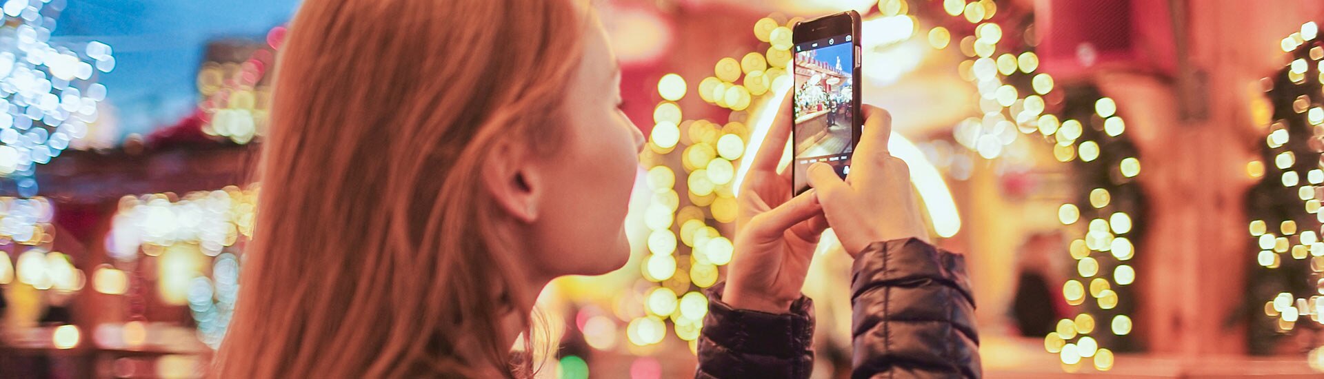 Horizonal close-up of woman using cell phone to photograph bright Christmas lights in Pigeon Forge, Smoky Mountains, TN.
