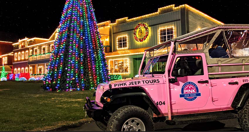 Side view of Pink Jeep Wrangler with guests seated in back, parked in front of the brightly lit Dolly Parton's Stampede at Christmas time.