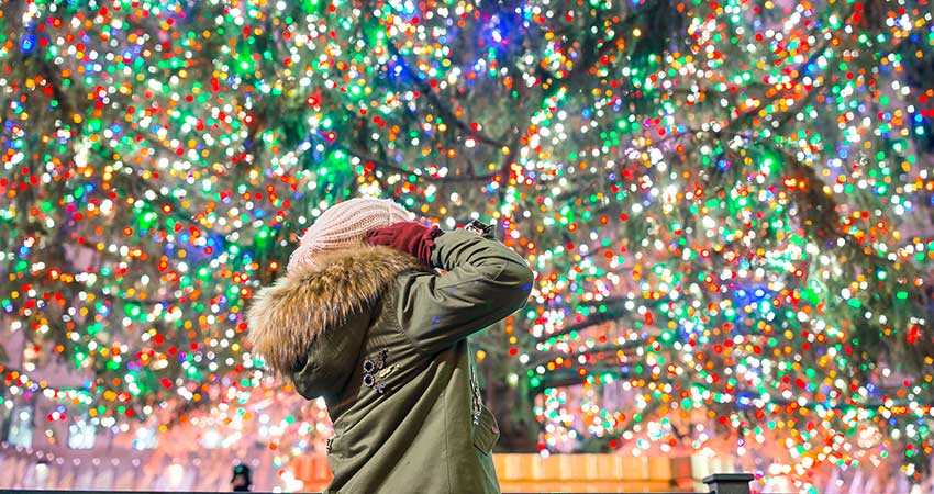 Happy girl with mittens holding ears, looking up at thousands of multicolored lights on a giant Smoky Mountains Christmas tree.